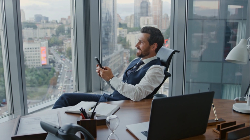 Image of a man in an office, looking at his phone, with a laptop and desk items, representing functional goals in a performance review
