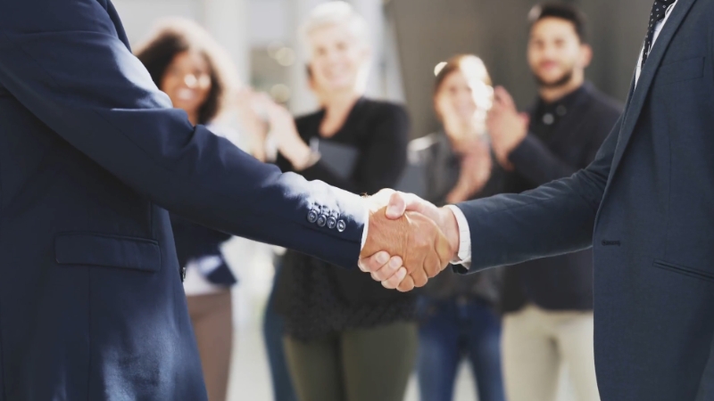 Image of two people shaking hands, with others clapping in the background