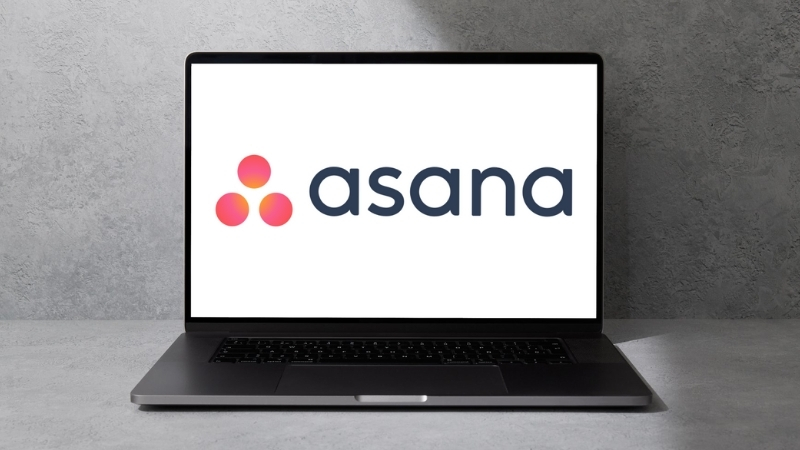 A laptop shows the Asana logo on screen