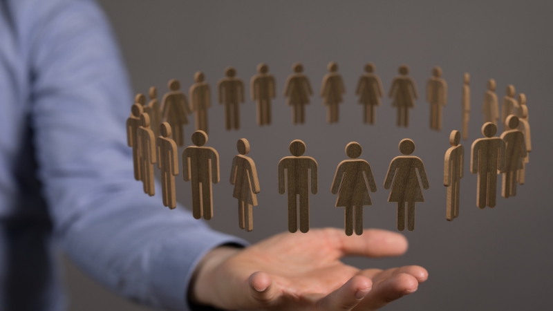 A hand holding a circle of wooden human figures representing teamwork and HR quotes on growth and resilience