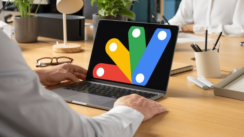 A person using a laptop with the Google Apps Script logo on the screen in a modern office environment