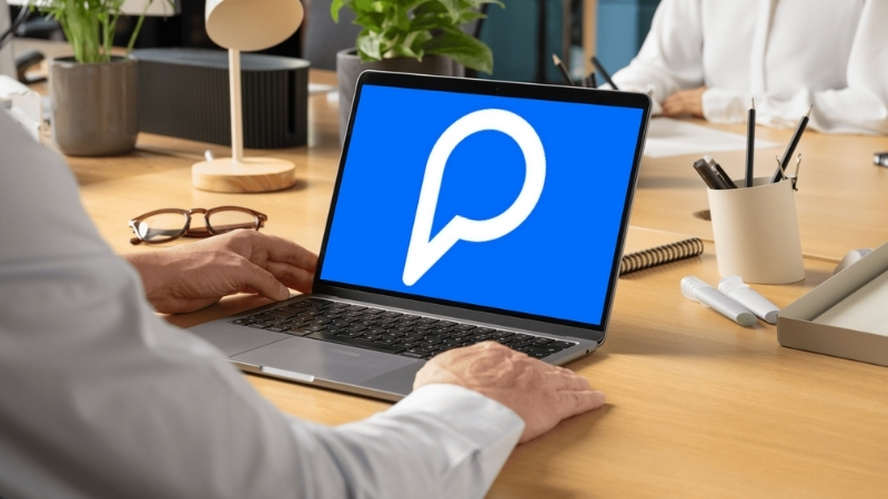 A person viewing the Peergrade logo on a laptop screen in a shared office workspace