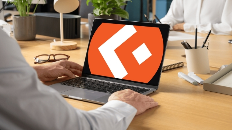 A person using a laptop with the Primalogik logo on the screen in a clean, modern office environment