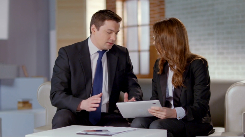 A man and a woman in business attire are discussing a performance review while looking at a tablet