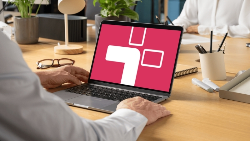A person using a laptop with the Teamflect logo displayed on the screen in a modern office workspace