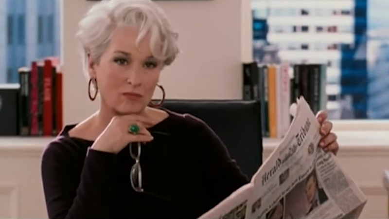 Miranda Priestly sits at her desk holding a newspaper, giving a sharp look in a scene from The Devil Wears Prada (2006)