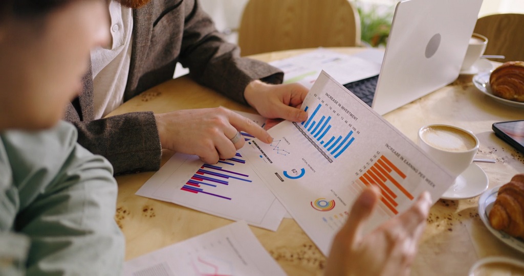 Close-up of professionals analyzing performance charts and business data at a café, focusing on HR investment and earnings KPIs
